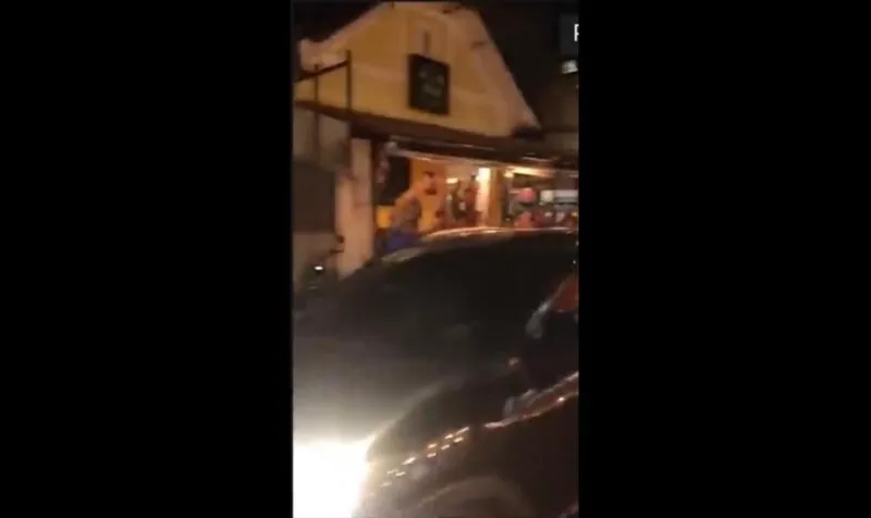 No vídeo, é possível ver uma mulher sentada no vidro fazendo gestos com a mão e o motorista do carro atirando para cima. No carro, há um adesivo da campanha de Jair Bolsonaro no vidro