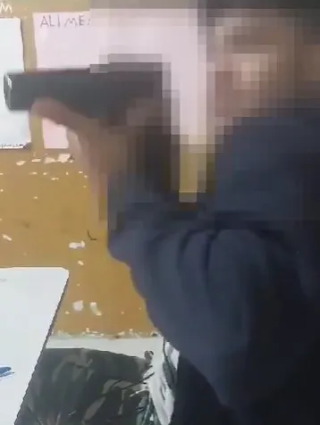 Nas imagens, um aluno aparece exibindo uma pistola e depois de 'brincar' com o armamento, aponta para a professora