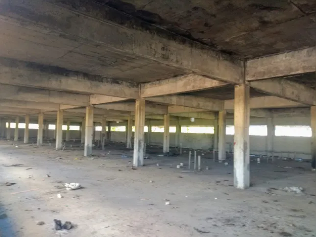 Nesta imagem, ao centro, é possível ver que um morador de rua dorme enrolado em um cobertor cinza no local que seria a base da construção da maternidade 