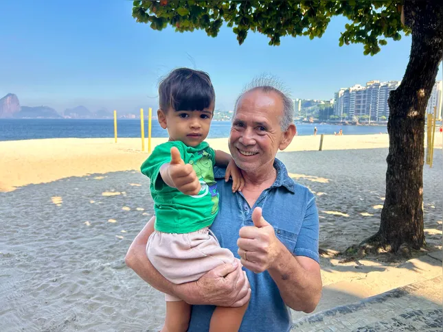 Pedro Augusto e o neto Théo Aquiama, caminhando juntos na praia
