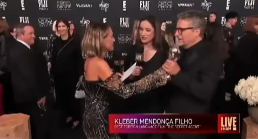 Kleber Mendonça Filho recebendo o prêmio durante o tapete vermelho, ao lado de sua esposa, Emilie Lesclaux