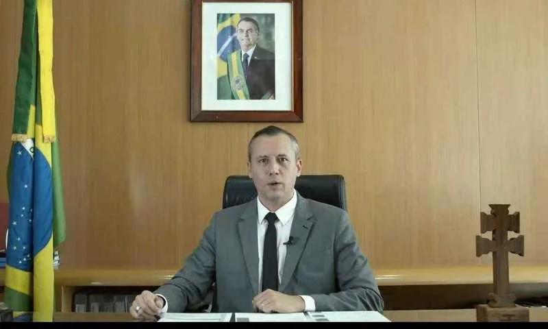 No vídeo, o secretário aparece em seu gabinete com a foto do presidente e a bandeira do Brasil.